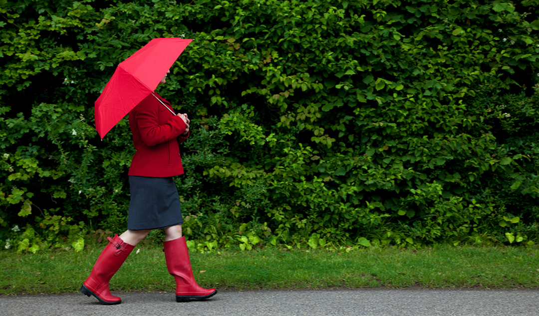 Photo of a woman in red walking along a road with her umbrella u